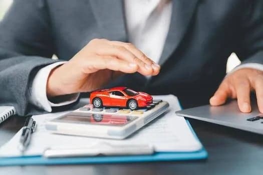A hand shielding a car beside a calculator, representing affordable protection