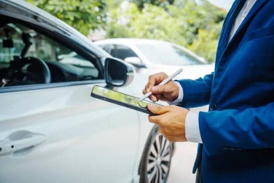 An insurance advisor inspecting a vehicle with a tablet